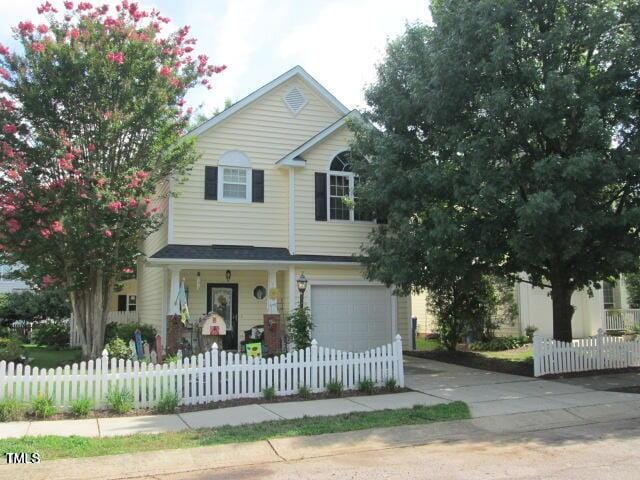 traditional-style house featuring a fenced front yard, an attached garage, and concrete driveway