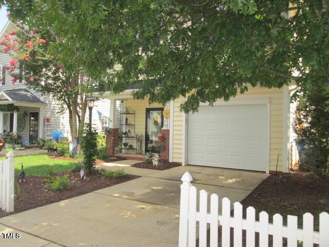 view of property hidden behind natural elements with driveway and fence