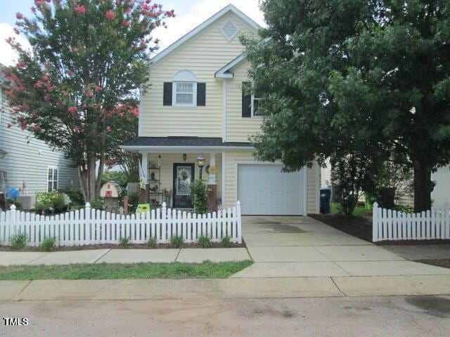 traditional-style home featuring a fenced front yard, driveway, a porch, and a garage