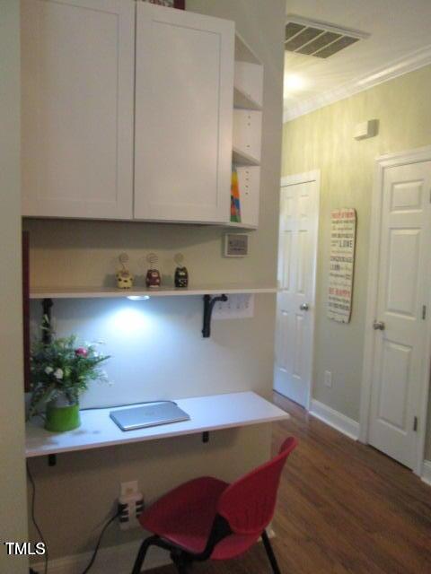 office area with wood finished floors, visible vents, built in desk, and baseboards