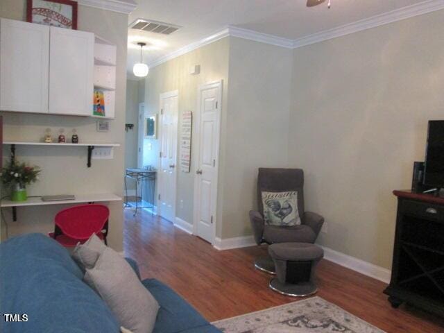 living area with a ceiling fan, baseboards, wood finished floors, visible vents, and ornamental molding