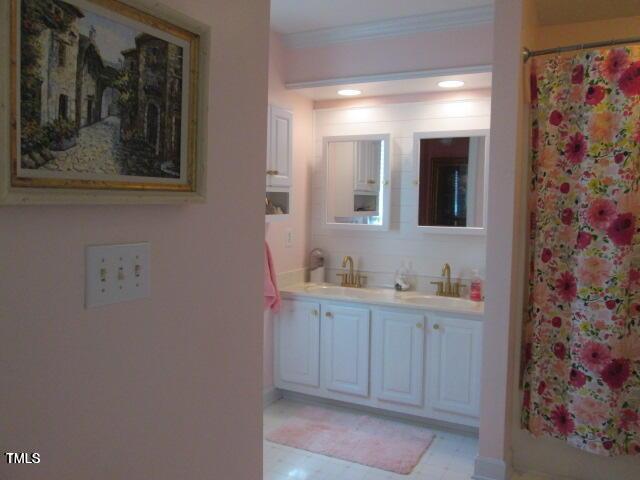 full bath with a shower with curtain, double vanity, ornamental molding, and a sink