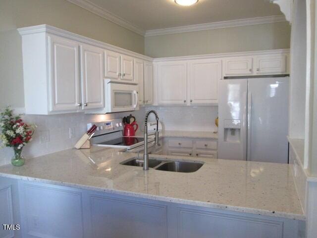 kitchen featuring white appliances, light stone countertops, a peninsula, and a sink