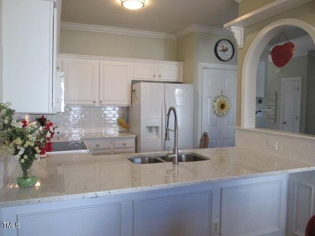 kitchen featuring crown molding, light stone countertops, decorative backsplash, a peninsula, and white refrigerator with ice dispenser