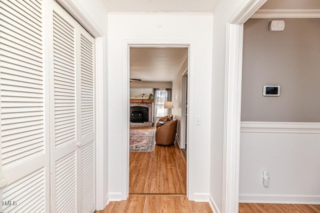 hallway with light wood-style flooring, baseboards, and ornamental molding