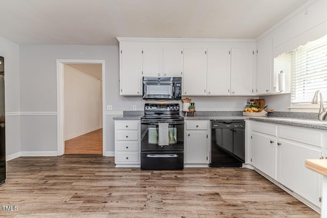 kitchen with white cabinetry, black appliances, light wood-style floors, and a sink