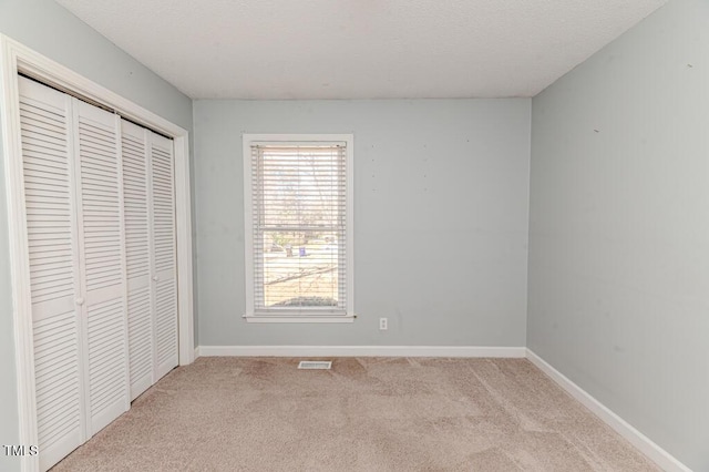 unfurnished bedroom featuring baseboards, visible vents, a closet, a textured ceiling, and carpet flooring