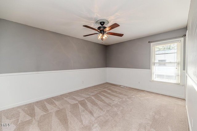 empty room with a wainscoted wall, a ceiling fan, and carpet flooring