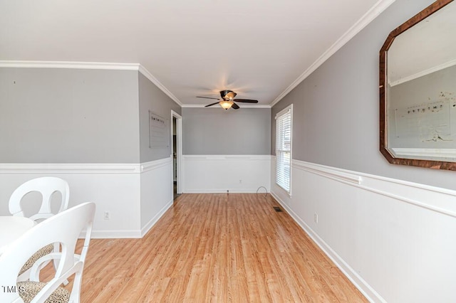 empty room with a wainscoted wall, ornamental molding, a ceiling fan, and wood finished floors