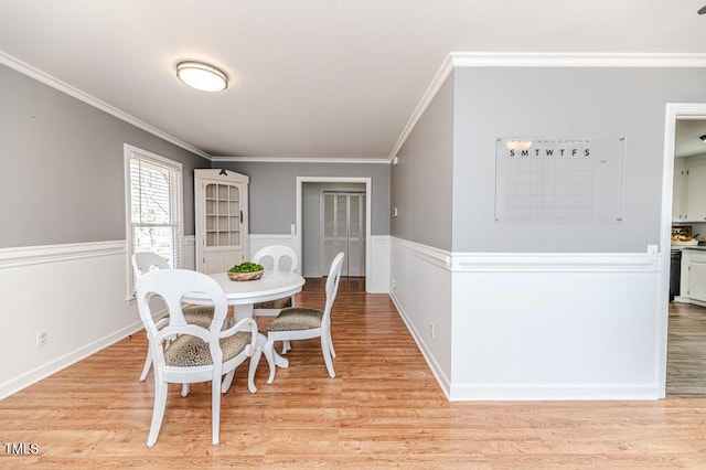 dining room with a wainscoted wall, light wood-style floors, and ornamental molding