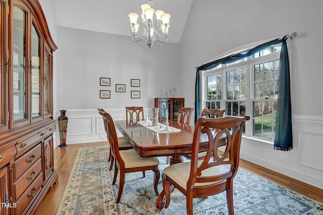 dining room featuring lofted ceiling, a notable chandelier, light wood-type flooring, and wainscoting