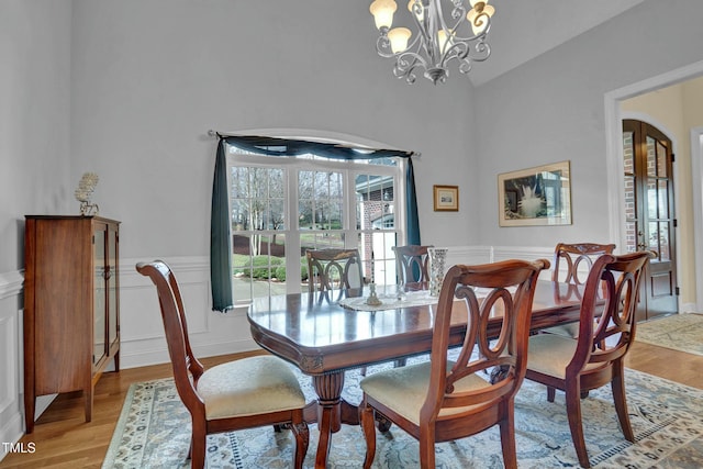 dining area with a wainscoted wall, arched walkways, a notable chandelier, and light wood finished floors