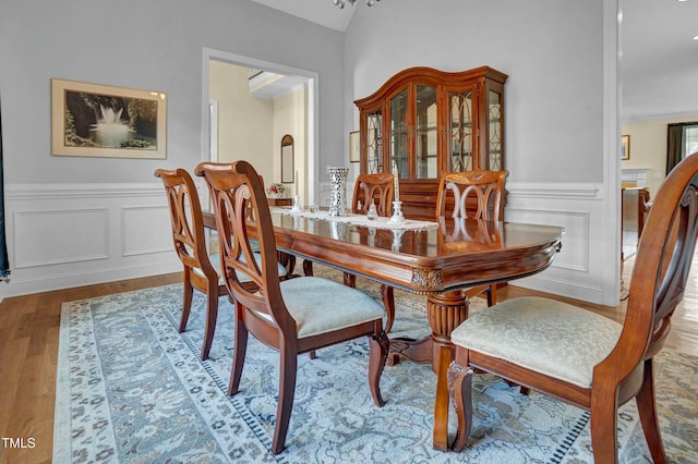 dining space with wood finished floors, wainscoting, and vaulted ceiling