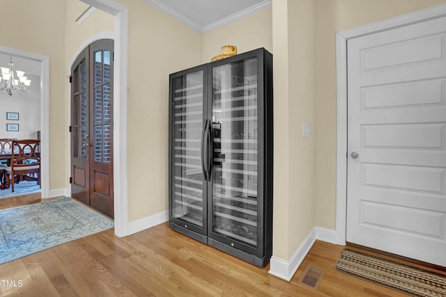 foyer with light wood-type flooring, an inviting chandelier, beverage cooler, and ornamental molding