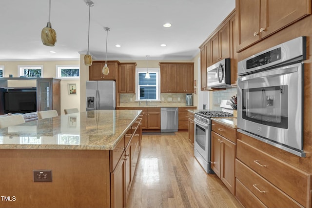 kitchen featuring light wood finished floors, light stone counters, decorative backsplash, appliances with stainless steel finishes, and brown cabinetry