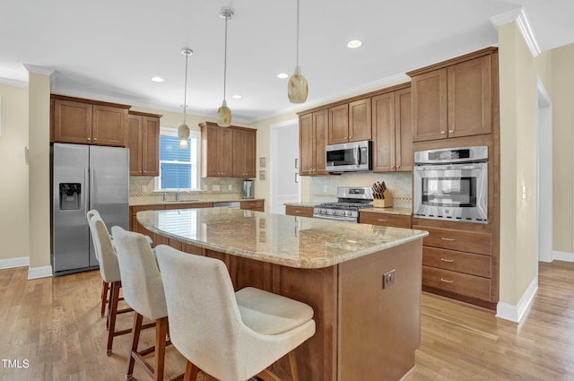 kitchen with crown molding, light wood-type flooring, a kitchen island, and stainless steel appliances