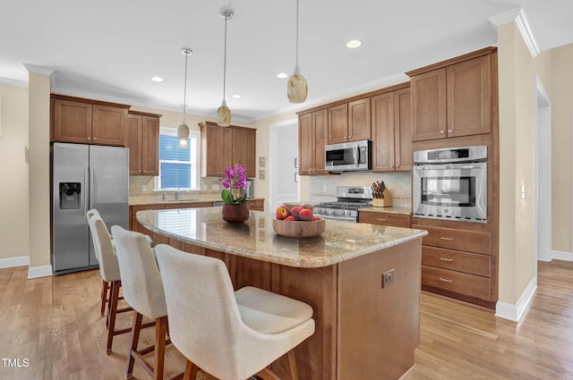 kitchen with stainless steel appliances, ornamental molding, a center island, and light wood finished floors