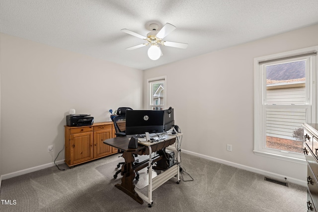 office space with visible vents, a ceiling fan, a textured ceiling, baseboards, and light colored carpet