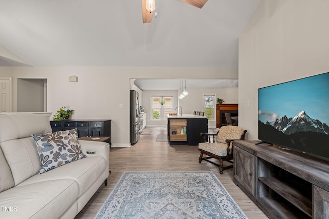 living room featuring a ceiling fan, light wood-type flooring, baseboards, and vaulted ceiling