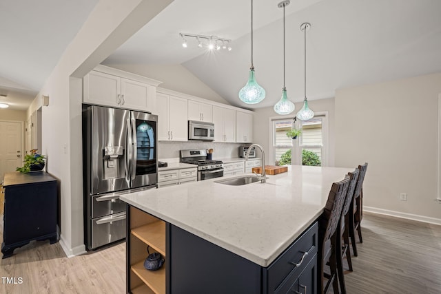 kitchen with a center island with sink, lofted ceiling, a sink, white cabinets, and appliances with stainless steel finishes