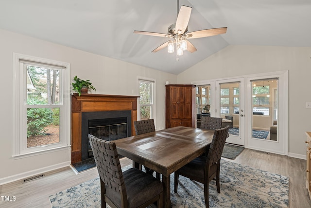 dining space with visible vents, light wood-style flooring, a glass covered fireplace, and vaulted ceiling