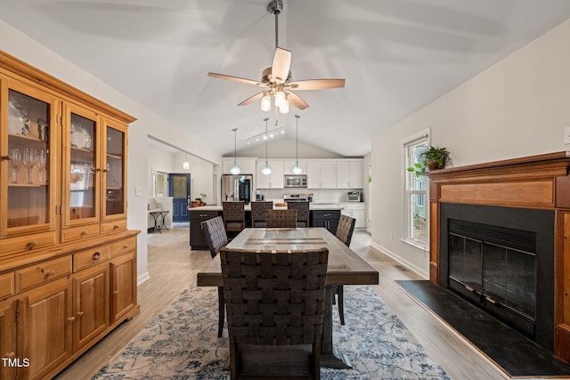 dining space featuring a glass covered fireplace, vaulted ceiling, light wood-type flooring, and ceiling fan