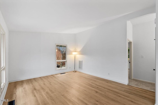 empty room with wood finished floors, visible vents, and baseboards