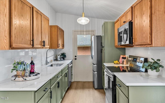 kitchen featuring stainless steel appliances, tasteful backsplash, green cabinets, light wood-style floors, and a sink