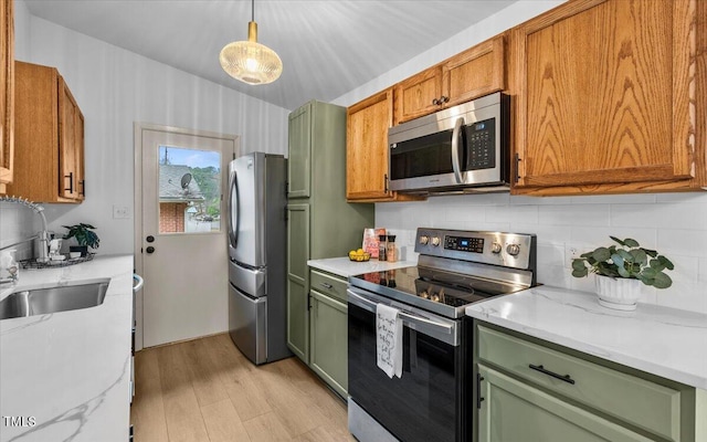 kitchen featuring appliances with stainless steel finishes, light wood-type flooring, backsplash, decorative light fixtures, and green cabinetry