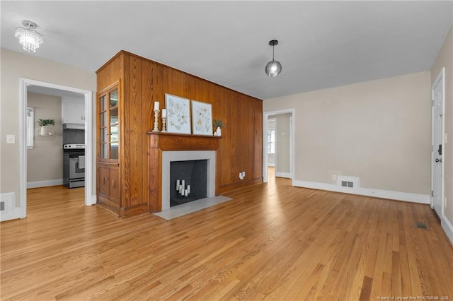 unfurnished living room with a fireplace with flush hearth, visible vents, wood walls, and light wood-style flooring