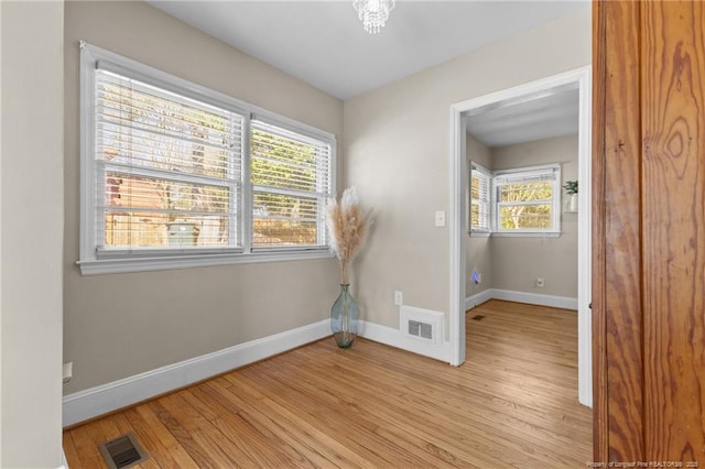 spare room with light wood-type flooring, visible vents, and baseboards