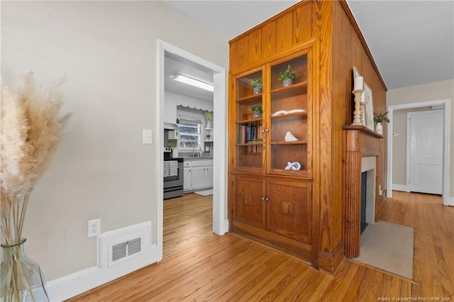 corridor with a sink, baseboards, visible vents, and wood finished floors