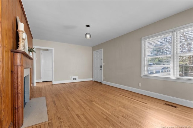 unfurnished living room with a fireplace with flush hearth, light wood-type flooring, visible vents, and baseboards