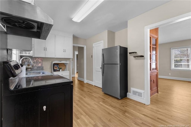 kitchen featuring black range with electric cooktop, a sink, visible vents, exhaust hood, and freestanding refrigerator