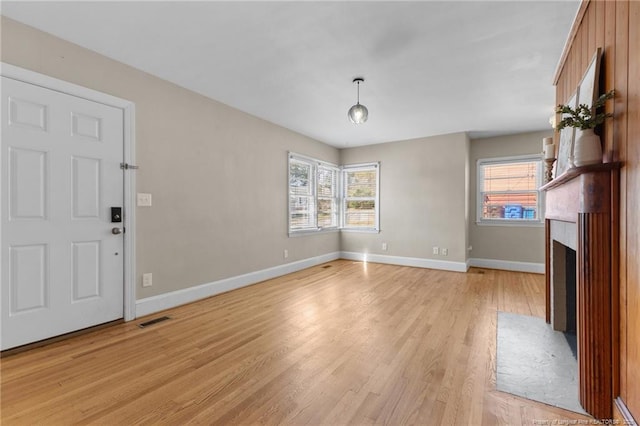 unfurnished living room featuring light wood finished floors, a fireplace with flush hearth, visible vents, and baseboards