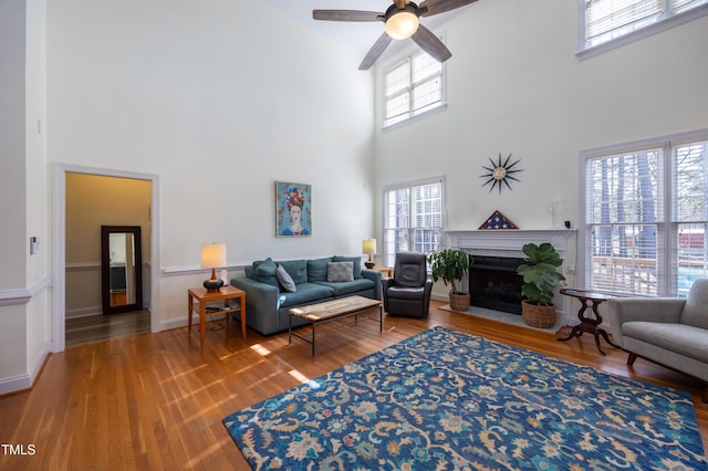 living area featuring ceiling fan, baseboards, a fireplace with flush hearth, and wood finished floors