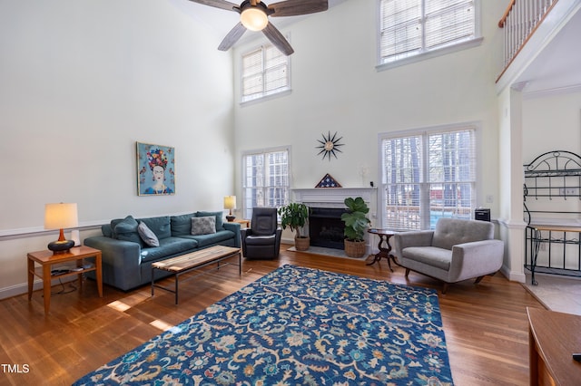 living area featuring a fireplace with flush hearth, ceiling fan, baseboards, and wood finished floors