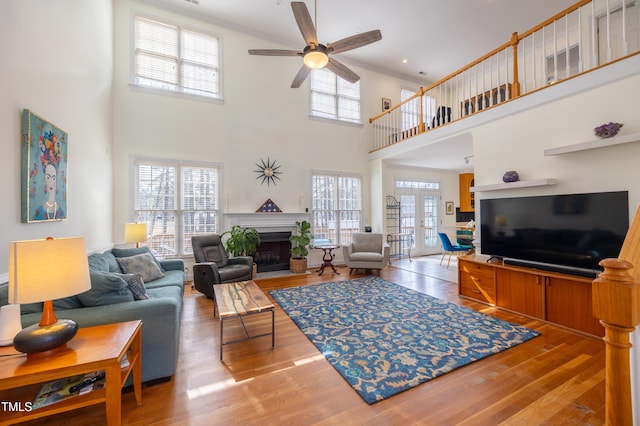 living area with ceiling fan, a fireplace with flush hearth, ornamental molding, french doors, and wood finished floors