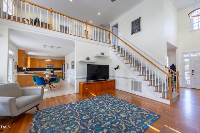 living room with visible vents, stairway, light wood-style floors, and ornamental molding