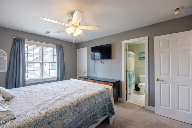 bedroom with a ceiling fan, visible vents, baseboards, light colored carpet, and connected bathroom