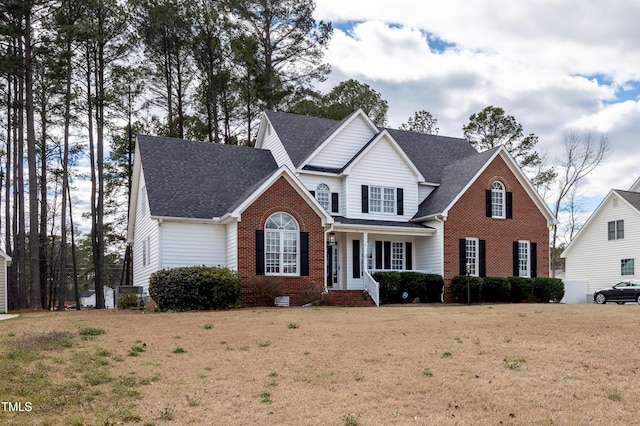 traditional home featuring brick siding, a front yard, and a shingled roof