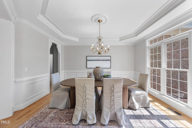 dining area featuring a wealth of natural light, visible vents, a tray ceiling, light wood-style floors, and an inviting chandelier