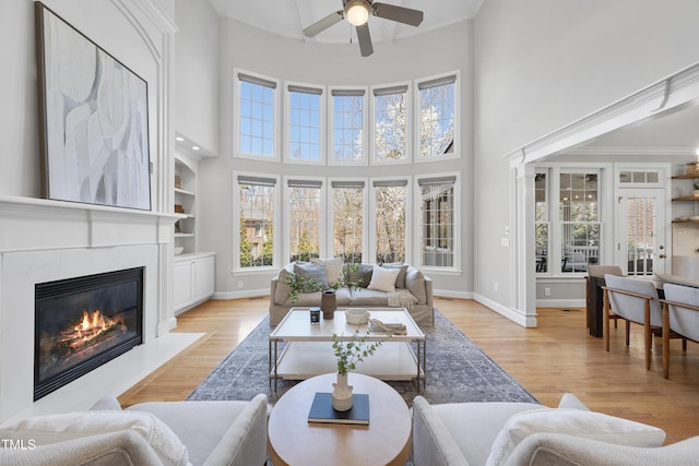 living room with a fireplace, baseboards, light wood-style floors, and a ceiling fan