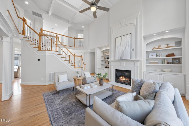 living room featuring a ceiling fan, visible vents, stairs, a glass covered fireplace, and light wood-type flooring