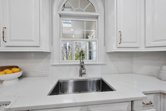 kitchen featuring backsplash, light stone countertops, white cabinetry, and a sink