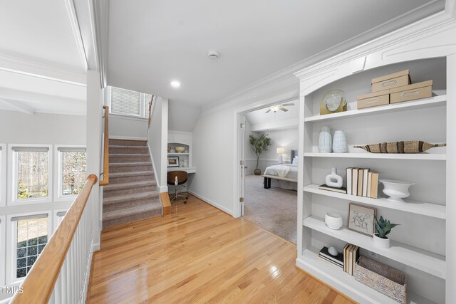 hall featuring built in shelves, ornamental molding, wood finished floors, baseboards, and stairs