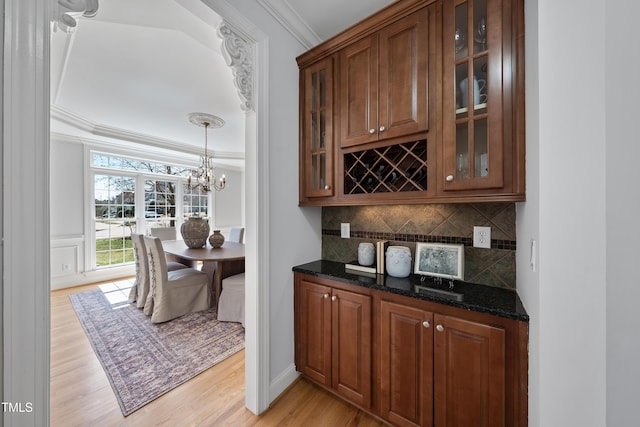 bar with light wood finished floors, backsplash, crown molding, pendant lighting, and an inviting chandelier