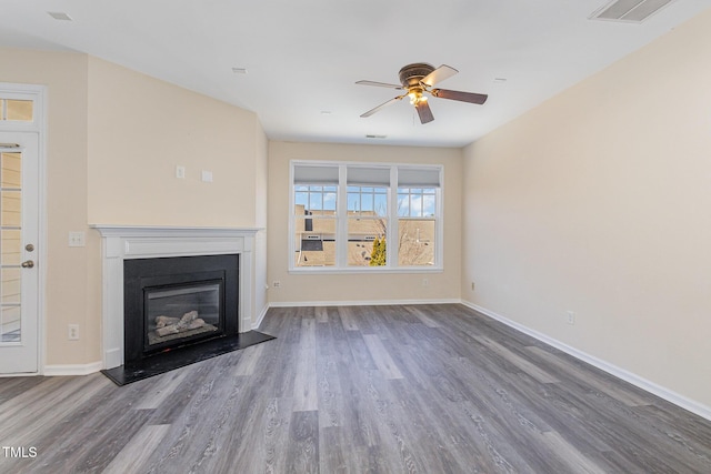 unfurnished living room featuring a glass covered fireplace, visible vents, baseboards, and wood finished floors