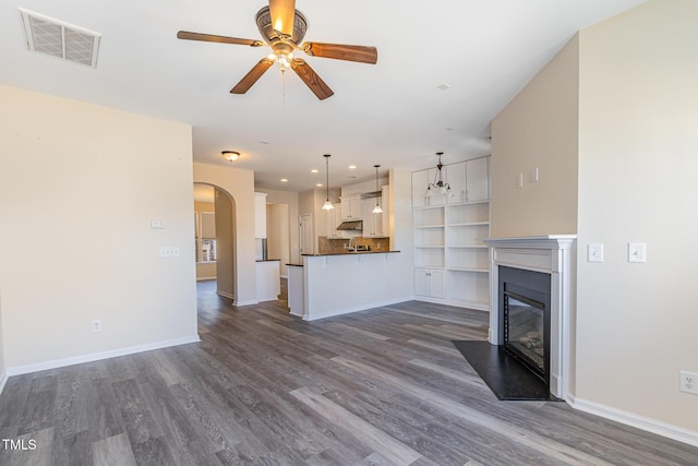 unfurnished living room with arched walkways, dark wood finished floors, visible vents, a fireplace with flush hearth, and baseboards