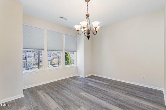 empty room with baseboards, visible vents, a chandelier, and wood finished floors